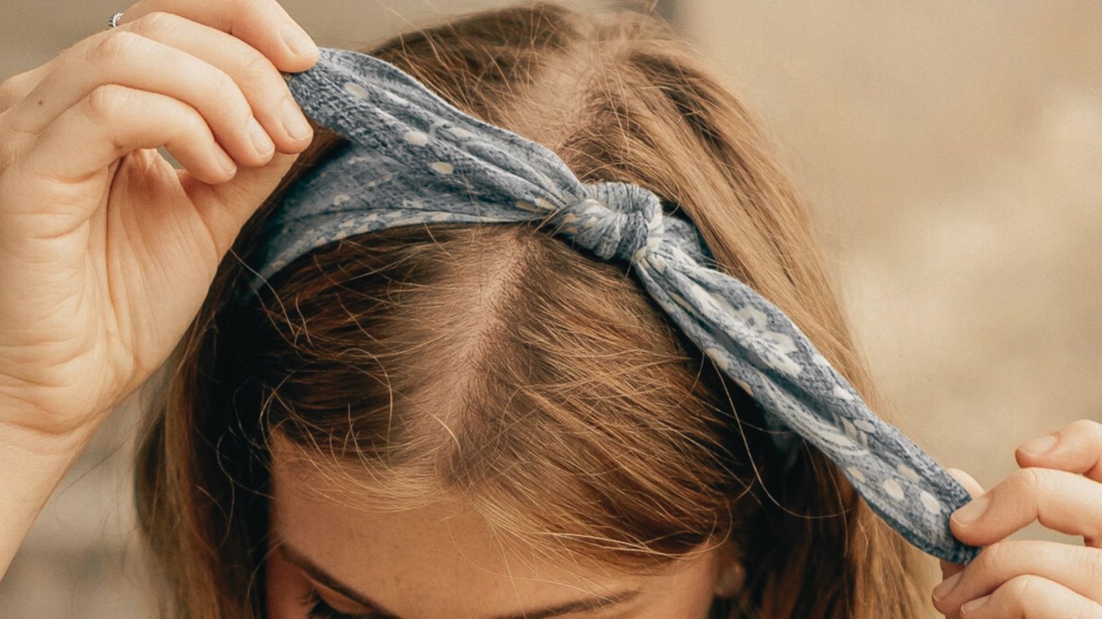 A woman ties her hair into a top knot, securing it with a colorful bandana.