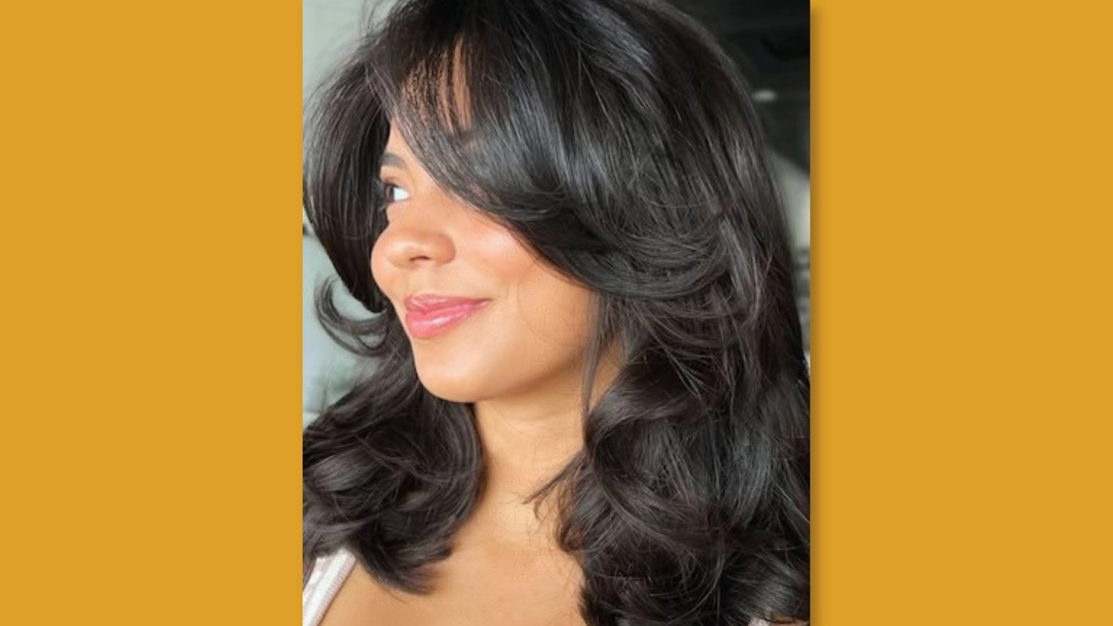 Low maintenance layered medium length haircut with voluminous curtain bangs and bouncy face-framing layers on glossy black hair for round face 
