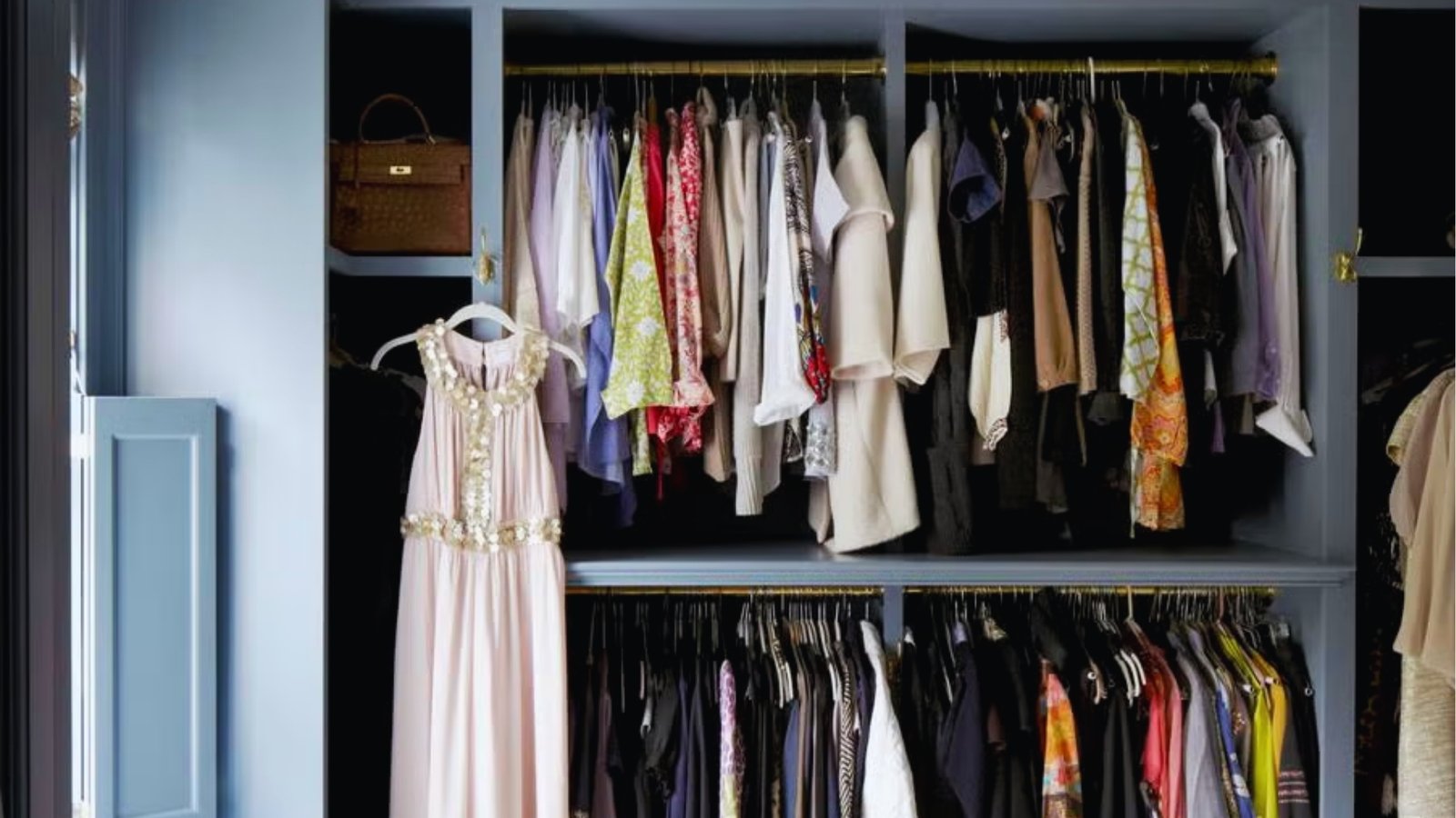 A neatly organized wardrobe with hanging clothes in various colors and styles. A pink dress is displayed outside. The setting exudes elegance and order.