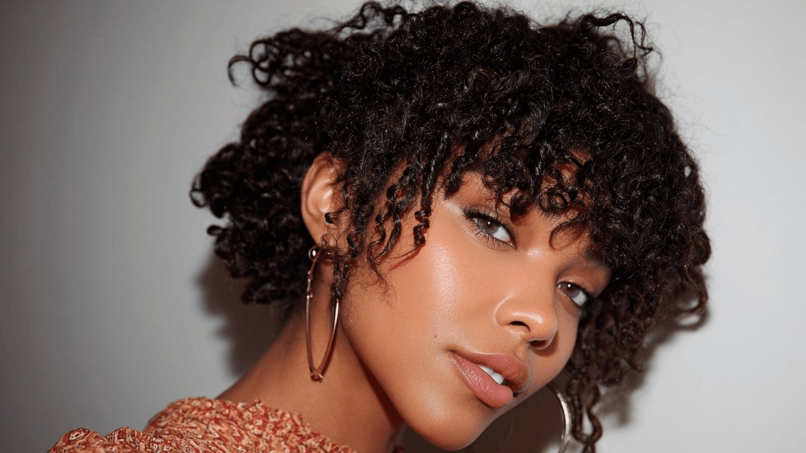 Woman with curly hair styled in an updo and soft curly bangs.
The coiled fringe frames the forehead with natural texture and volume.