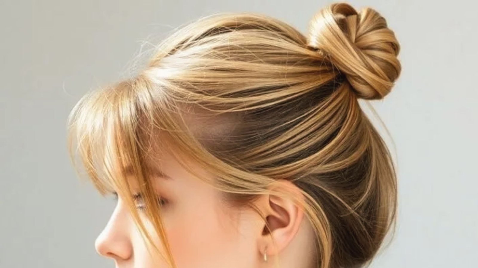 A woman with a messy bun hairstyle, featuring long bangs framing her face.