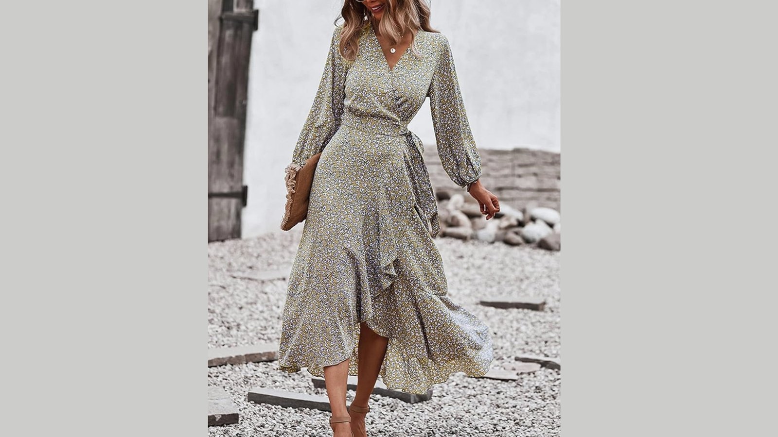 A woman in a floral wrap dress with long sleeves walks confidently on a gravel path. The outfit is stylish and elegant, conveying a relaxed, chic vibe.