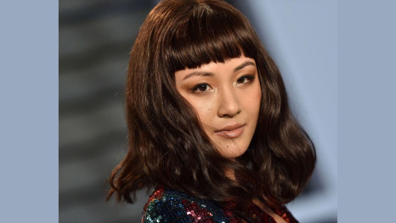 Woman with shoulder-length wavy brown hair and blunt baby bangs. The short, straight fringe cuts across the forehead above the eyebrows.