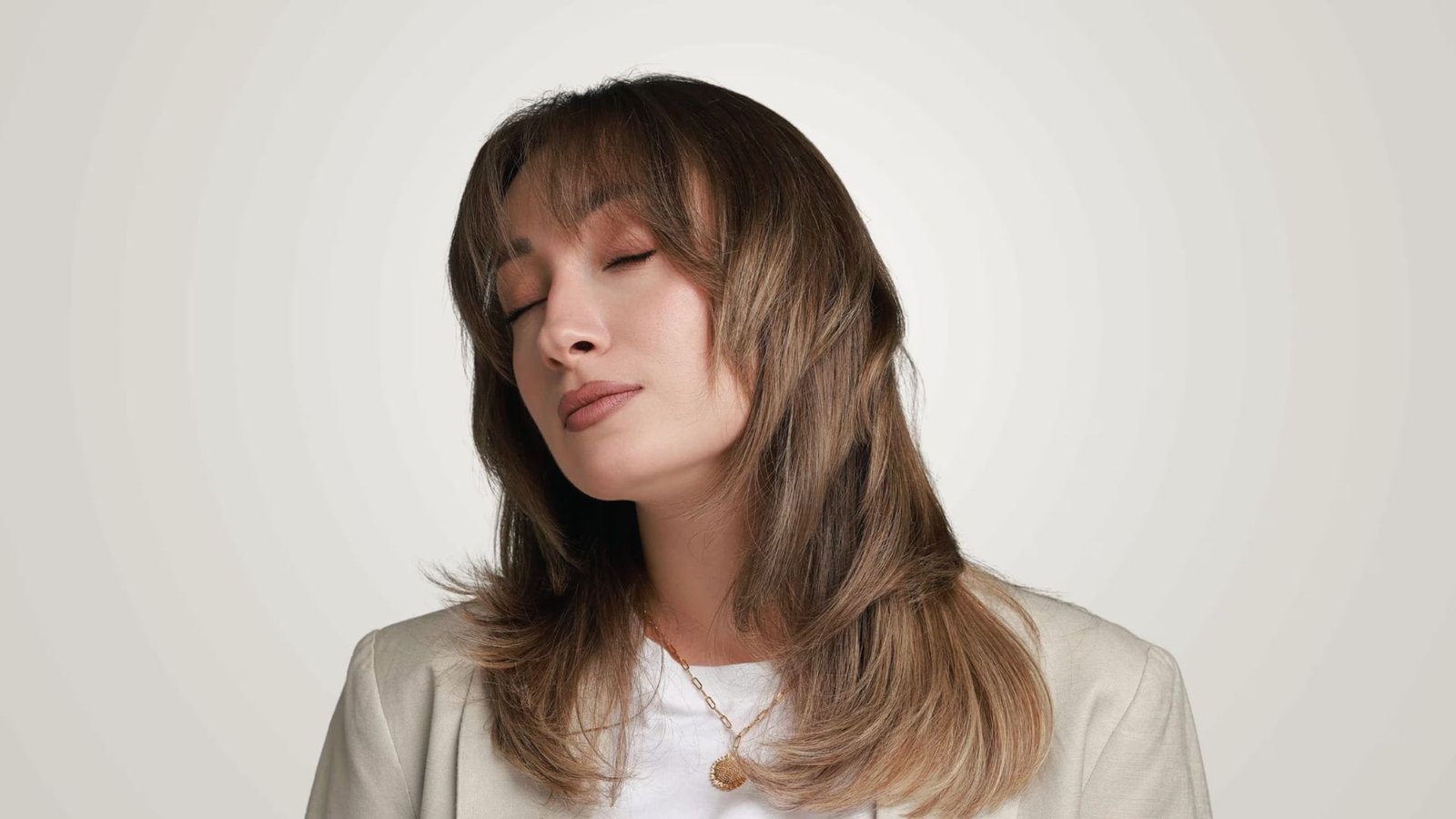 A woman with closed eyes and a tilted head, showcasing her C-Curl Butterfly Cut hairstyle.
