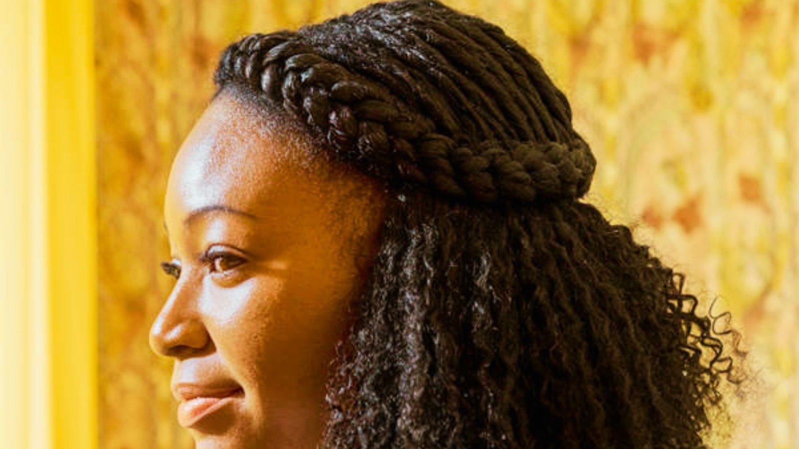 A woman with long curly hair styled in a braid, showcasing a half-up half-down hairstyle with Senegalese twists.