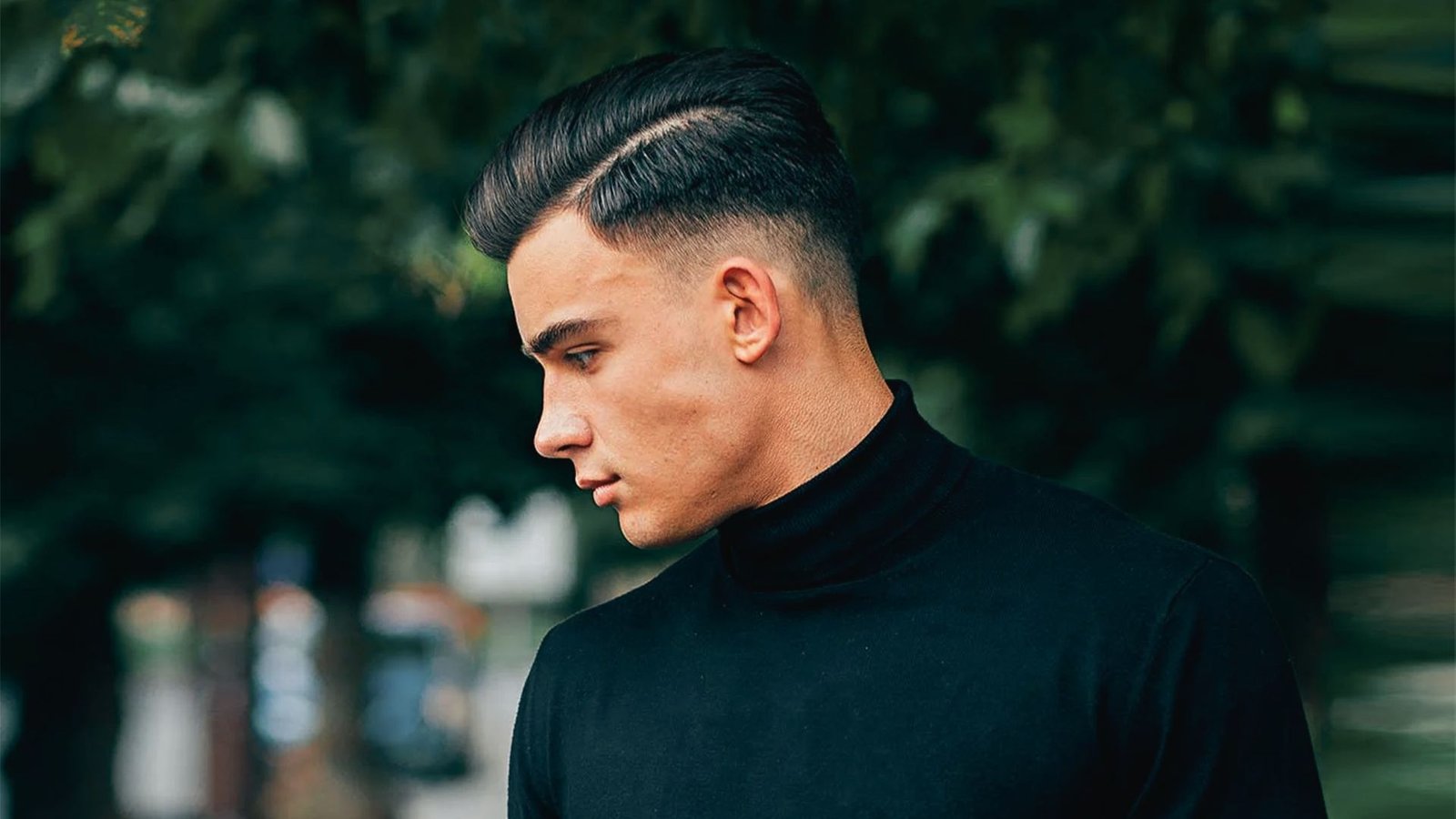 A man wearing a black turtleneck sweater with a comb over disconnected undercut fade hairstyle.