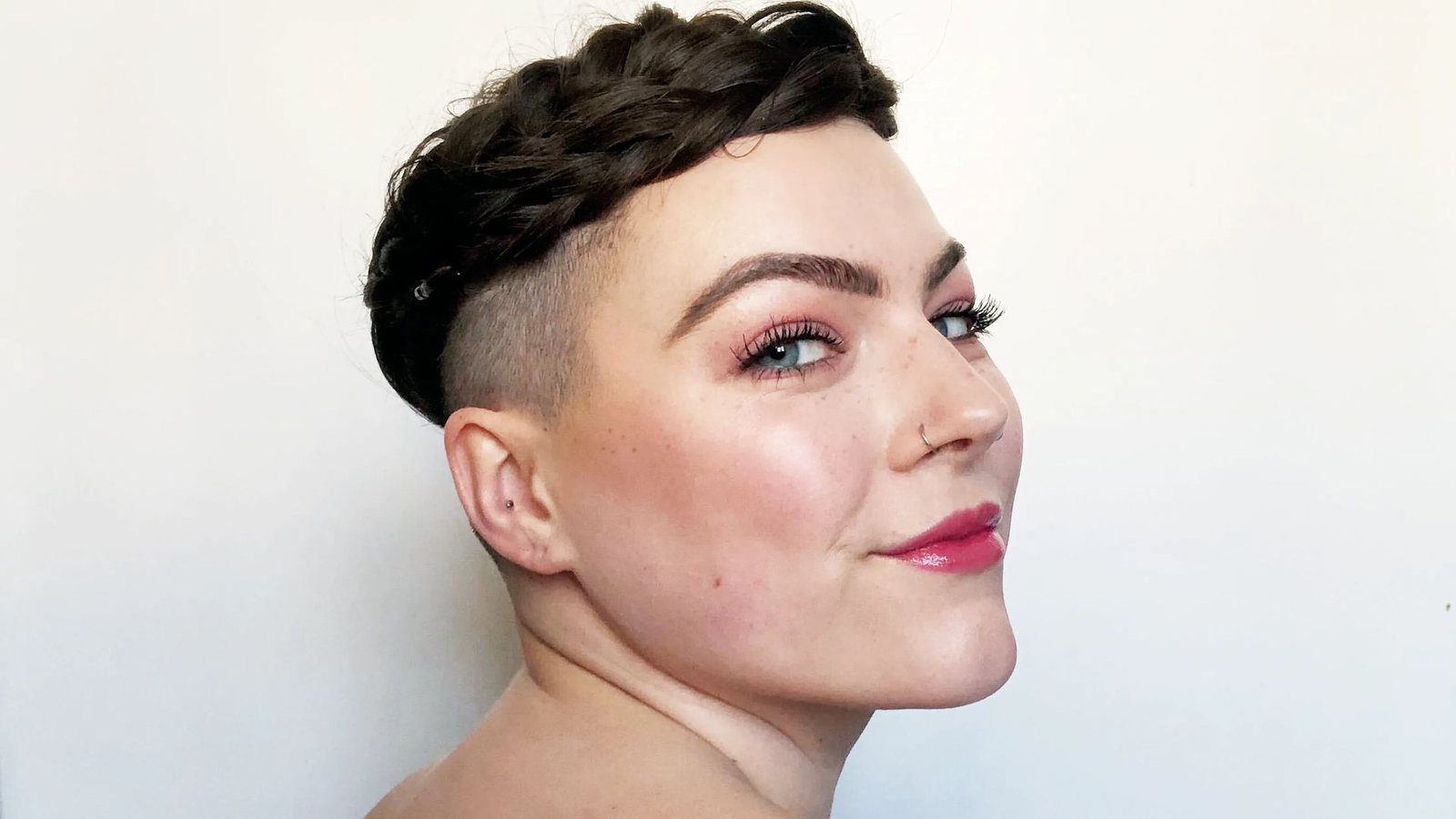 Close-up side view of a woman with dark hair styled in a braided crown and shaved undercut. Clean fade on the sides highlights the textured braid wrapped around the head.