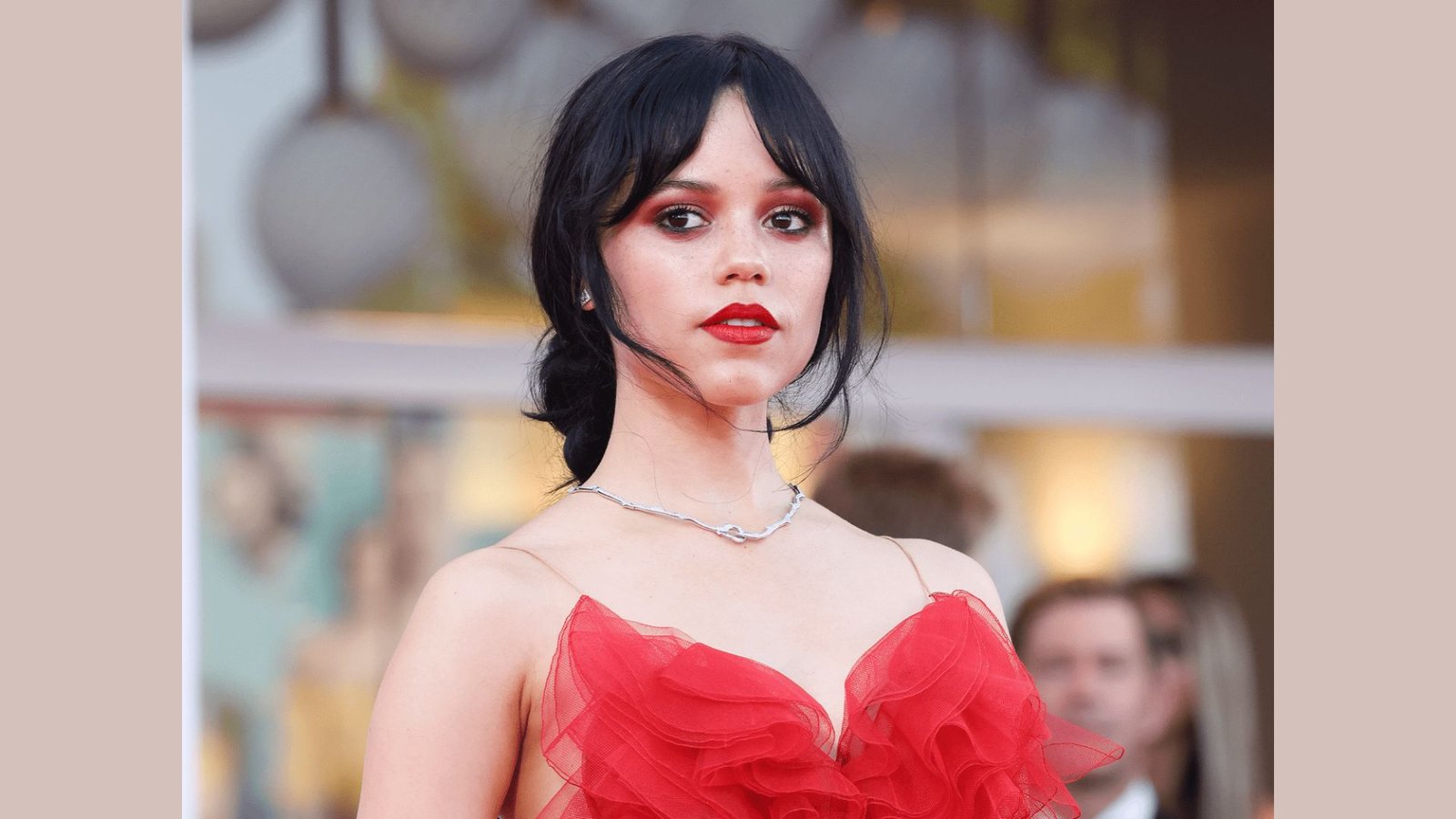 Woman in a red gown with dark hair pulled back and arched curtain bangs. The center-parted fringe frames the face and tapers toward the cheekbones.