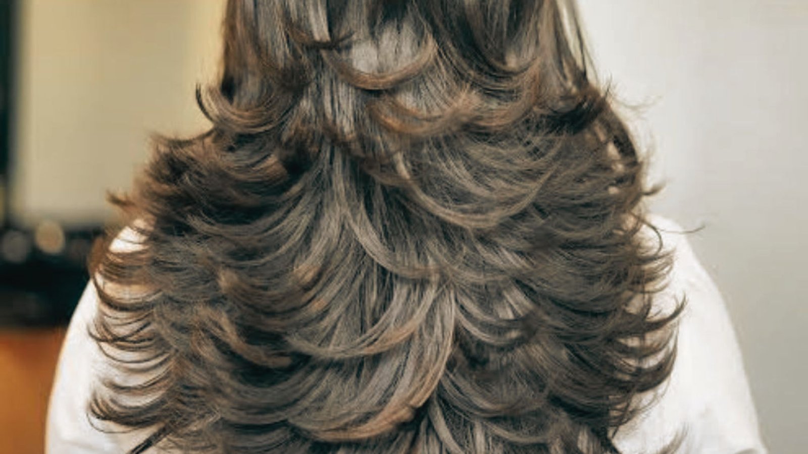 A woman with long, wavy hair showcasing a feathered butterfly cut in a salon setting.
