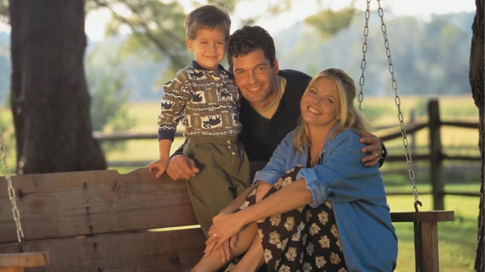 A family in 90s outfits joyfully sits on a swing in a sunny field, surrounded by green grass and wildflowers.