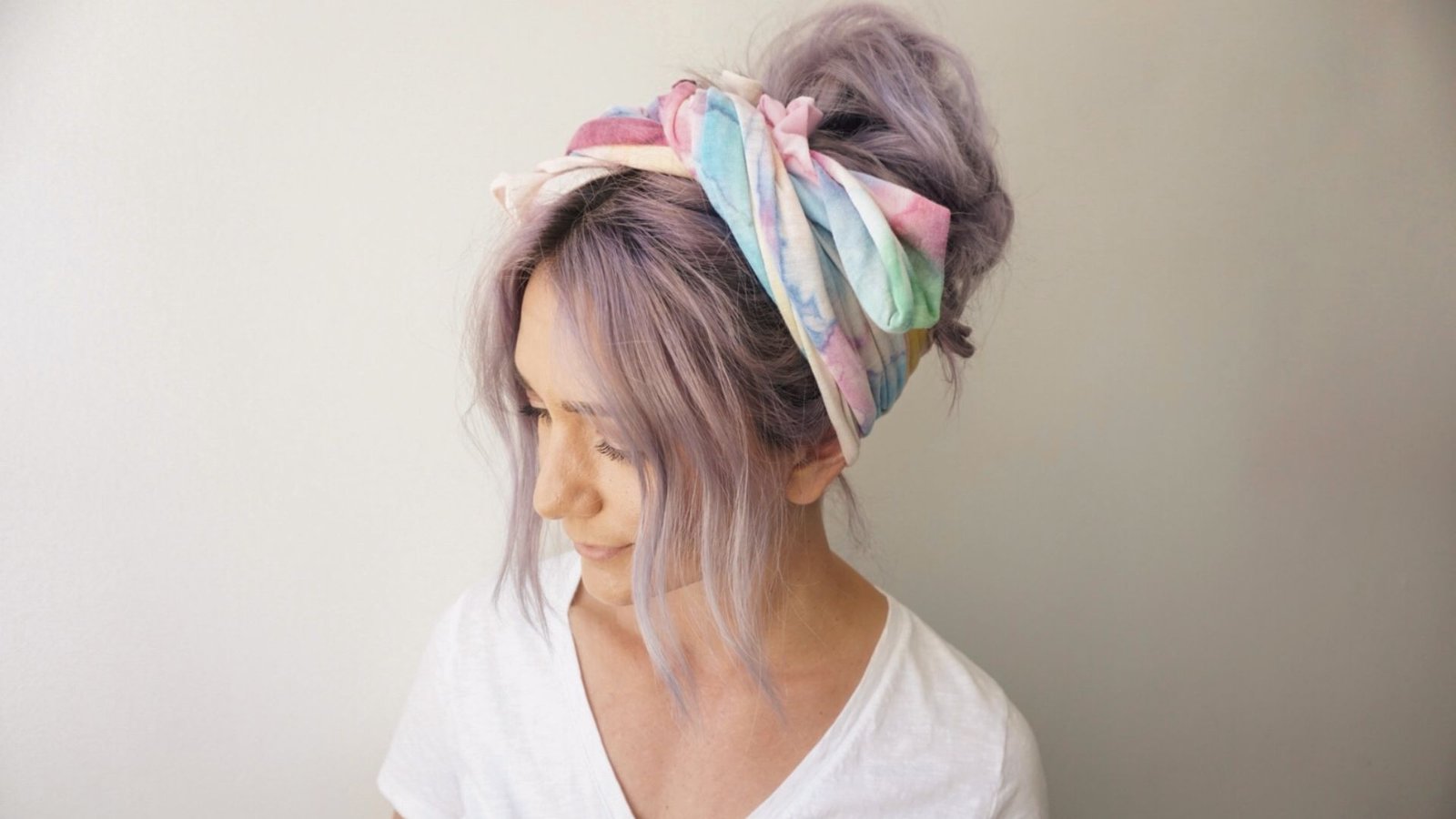 A woman with purple hair styled in a messy bun, wearing a scarf and bangs.