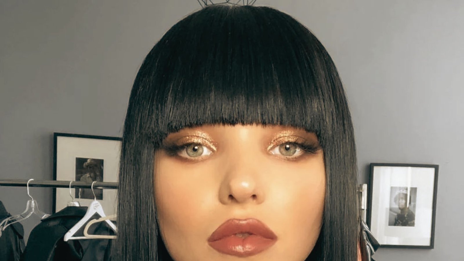 A woman with sleek straight black bob hair and blunt bangs, wearing bold red lipstick.