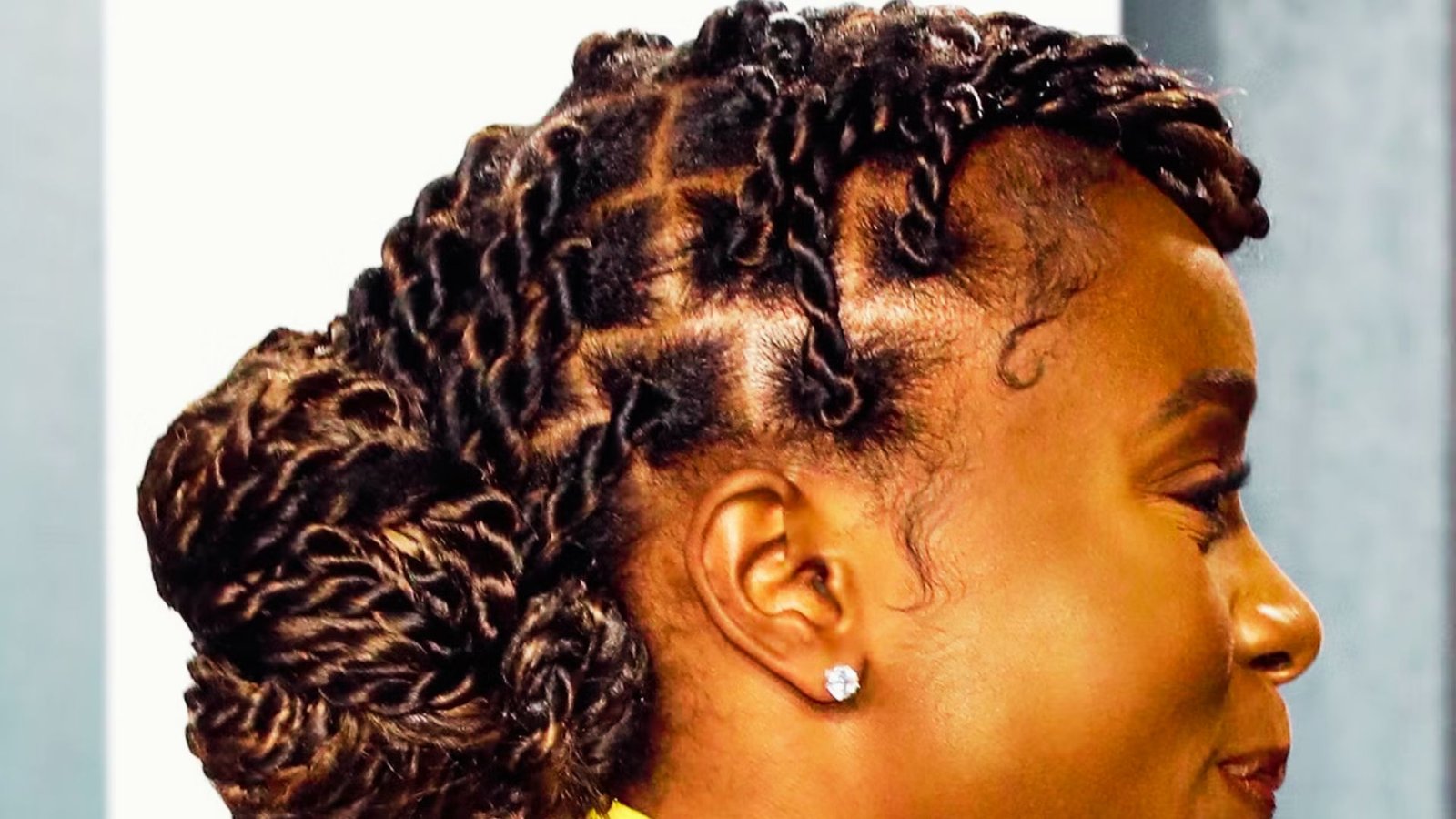 A woman with braids styled in a high bun, showcasing Senegalese twists with curls for a chic look.