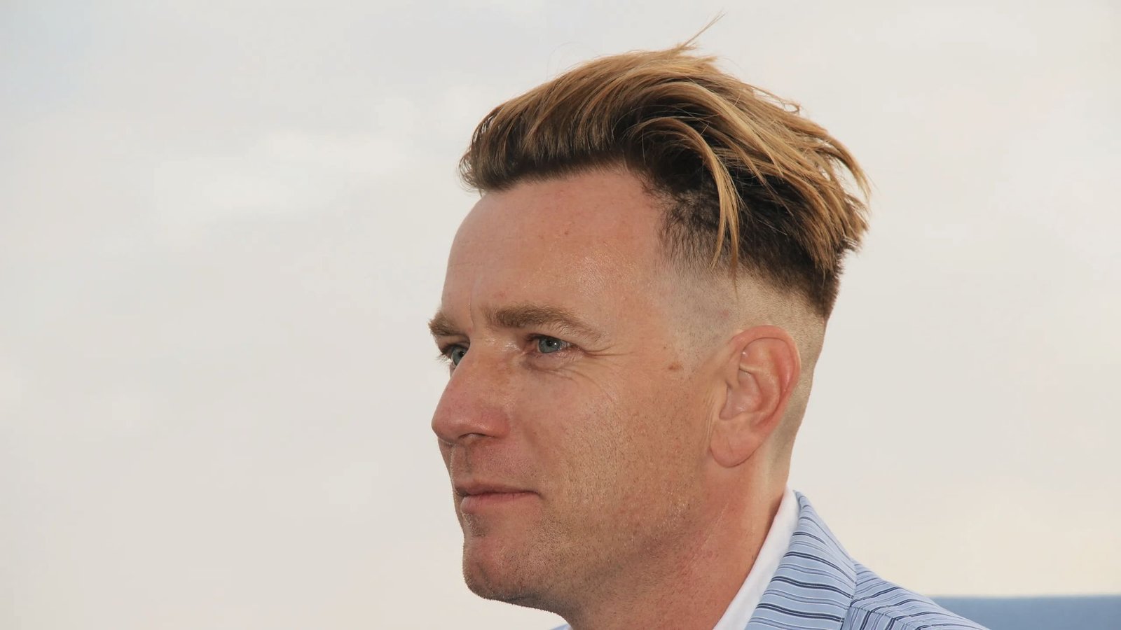 A man with a disconnected undercut fade hairstyle gazes thoughtfully to the side.