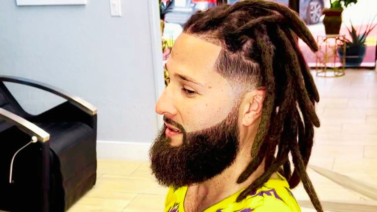 A man with a half-up half-down wicks hairstyle seated in a chair, displaying his stylish dreadlocks.