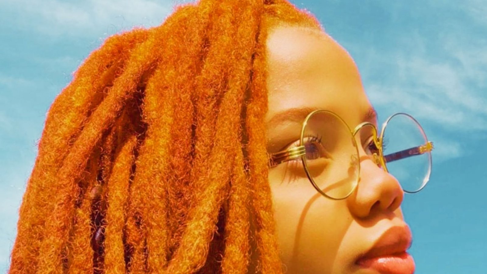 A young girl with orange dreadlocks, glasses, and a color-tipped wicks hairstyle.