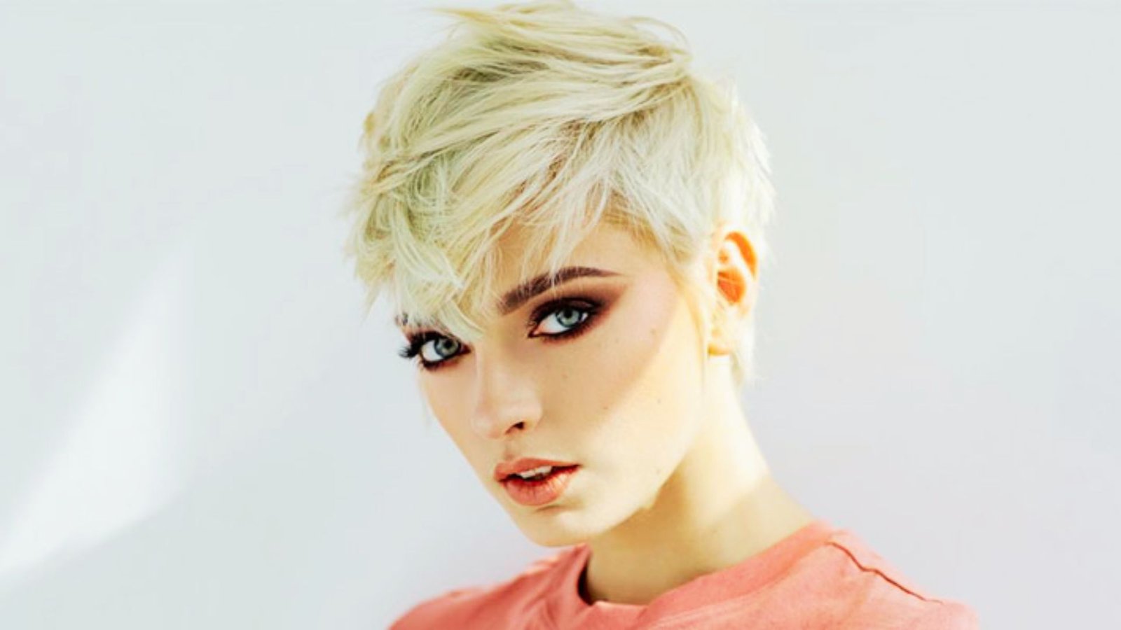 A woman with short blonde hair and blue eyes, showcasing a bold and edgy pixie cut hairstyle.