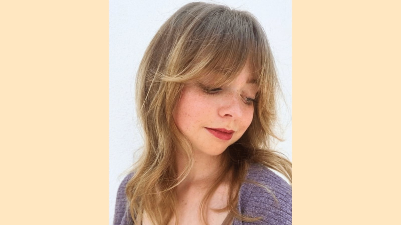 Medium-length wavy blonde layered haircut with soft wispy curtain bangs and tousled texture