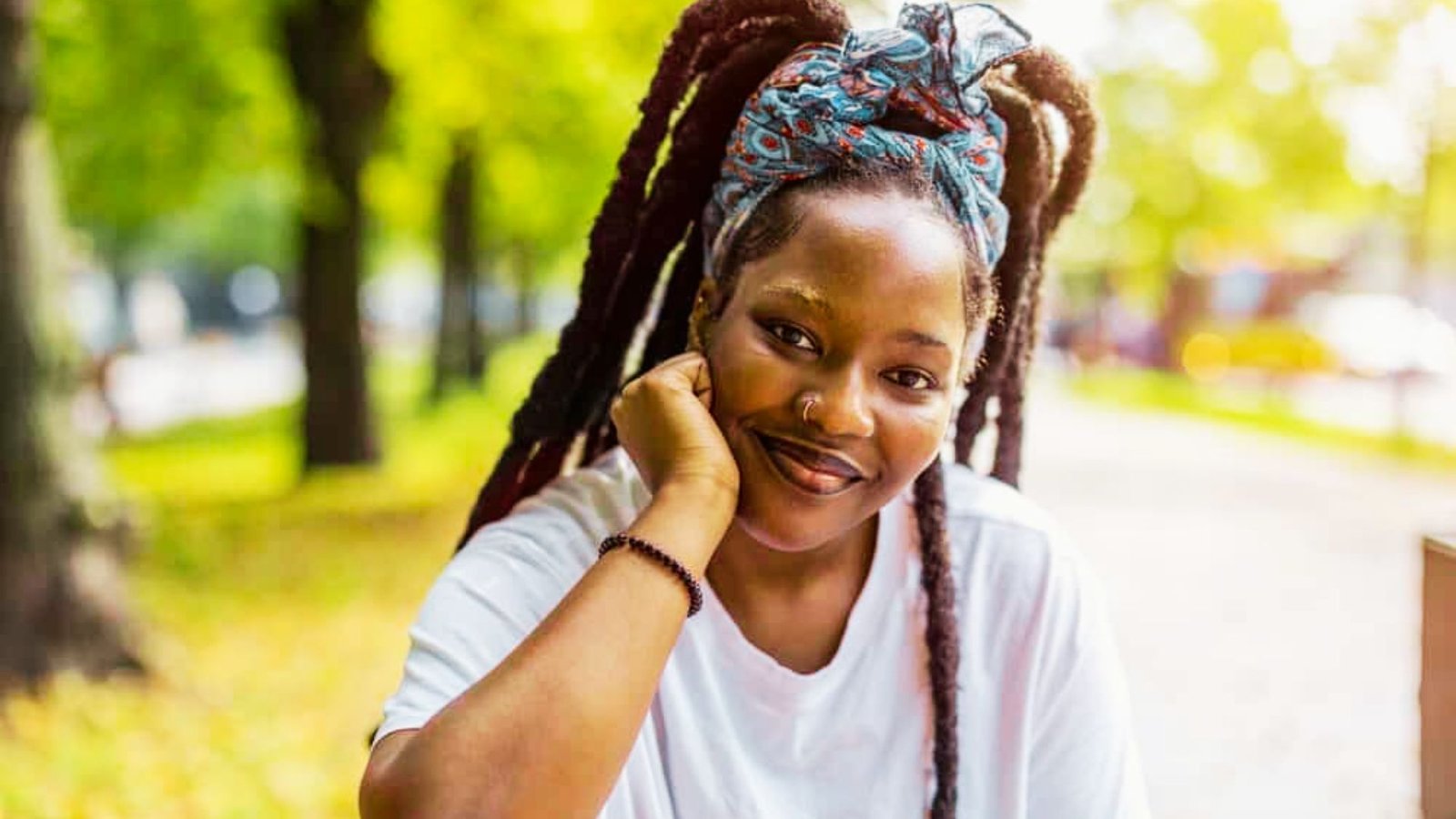 A woman with dreadlocks sits on a bench, showcasing the cultural significance of this hairstyle.