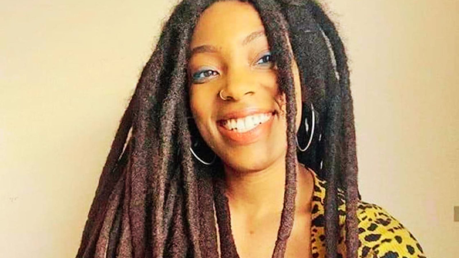 A woman with extra long dreadlocks smiles while wearing a stylish leopard print shirt.