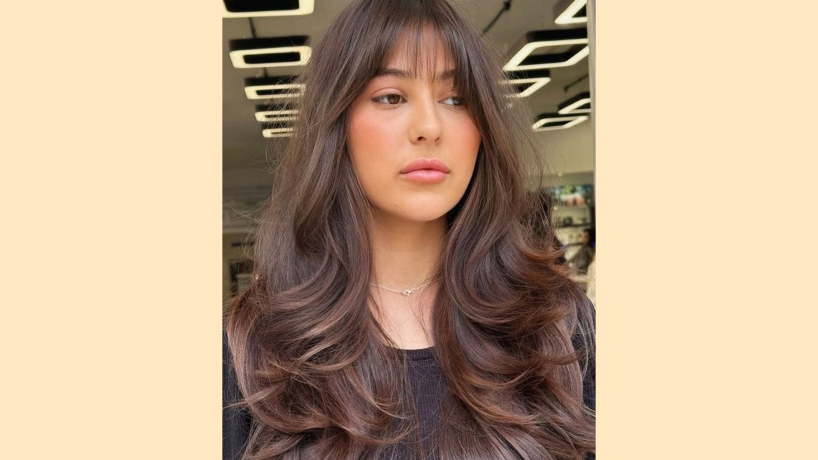 Wispy curtain bangs with soft face-framing layers on long wavy brunette hair in salon