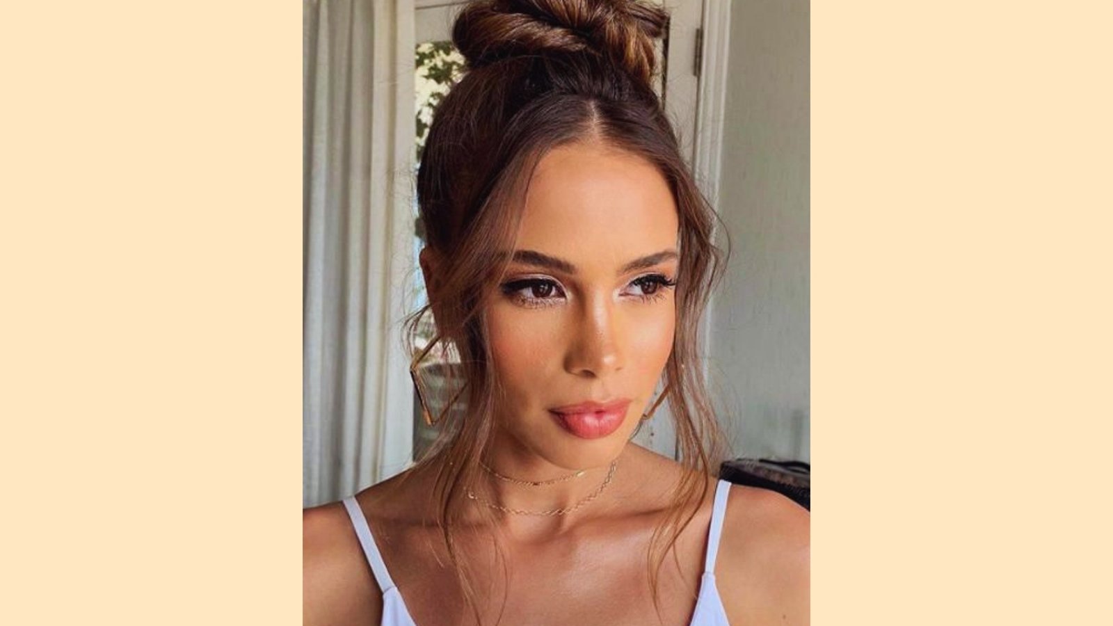 Messy high bun updo with wispy curtain bangs and soft face-framing tendrils on light brown highlighted hair