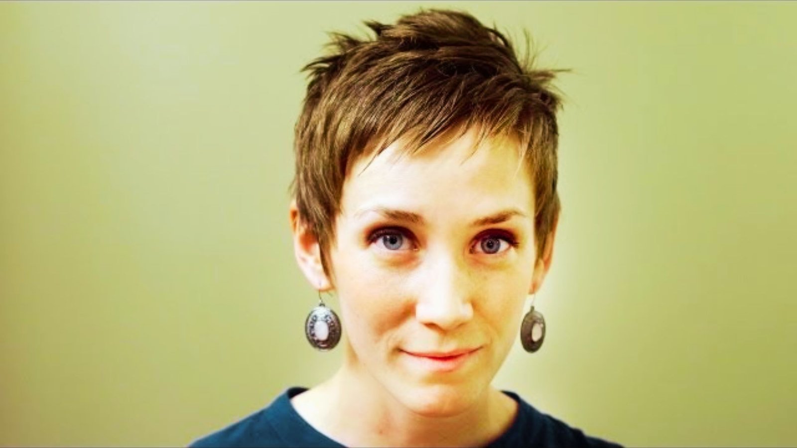 A woman with a micro spiky pixie cut and earrings, showcasing her short hair and stylish accessories.