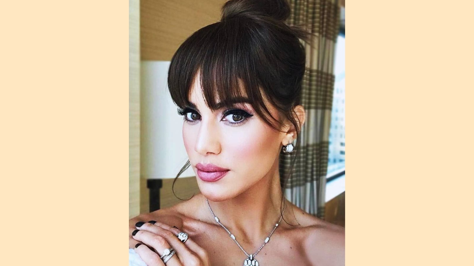 Sleek high bun updo with wispy piecey curtain bangs and soft side-swept framing on dark brown hair