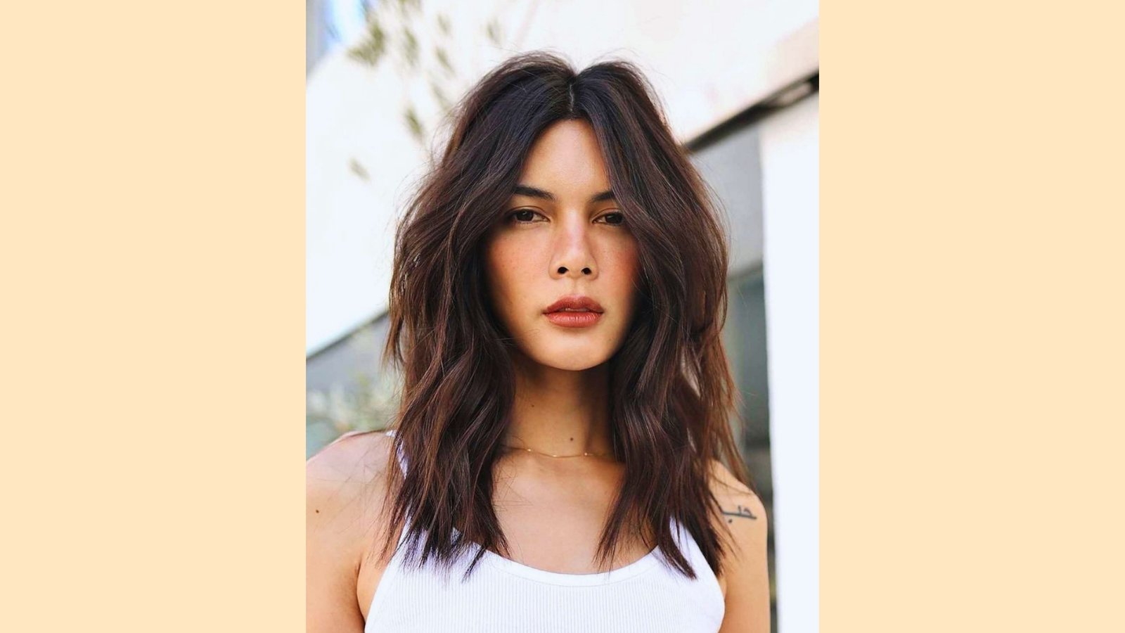 Medium-long wavy haircut with center-parted wispy curtain bangs and tousled texture on dark brunette hair