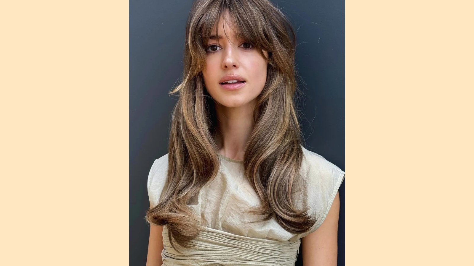 Long layered hairstyle with wispy curtain bangs and voluminous waves on blonde balayage hair