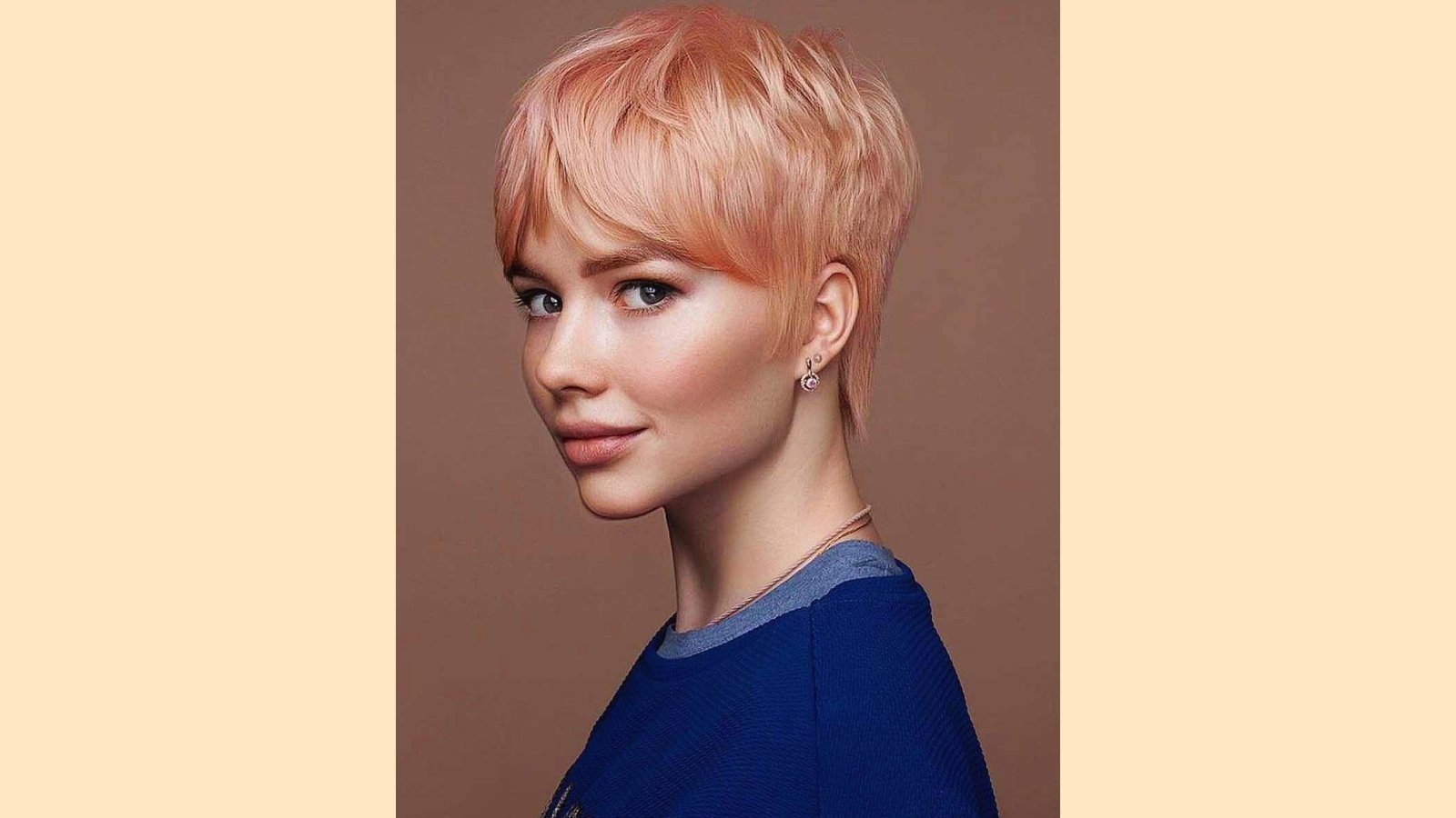 Short pixie cut with wispy curtain bangs and textured layers on pastel peach blonde hair