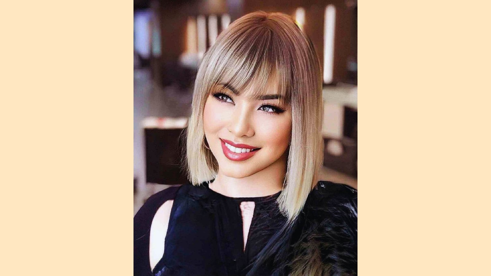 Shoulder-length straight blonde bob with wispy blunt bangs and subtle root shadow