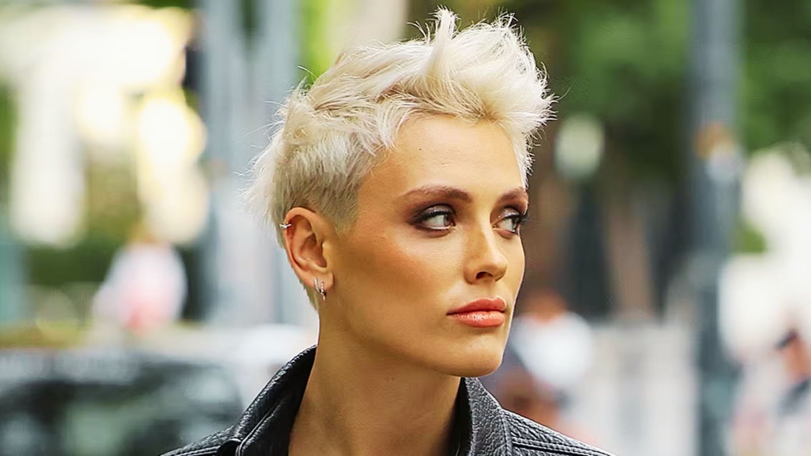 A woman with a disconnected undercut pixie cut, short blonde hair, wearing a black jacket.