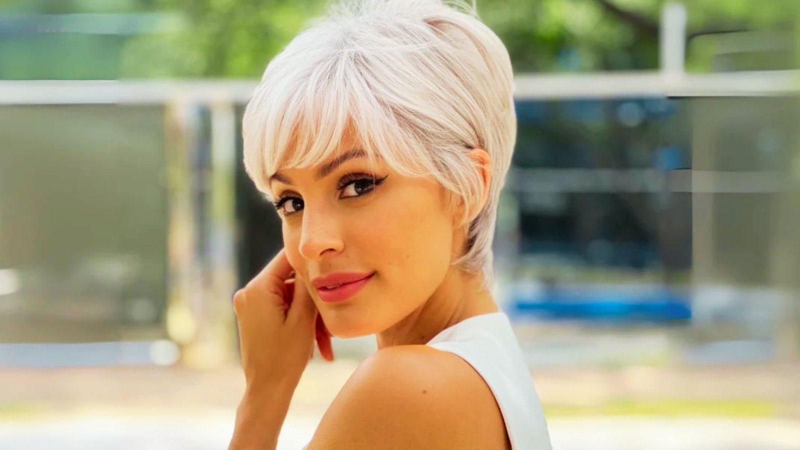 A woman with short white hair styled in a pixie cut, dressed in a white shirt.