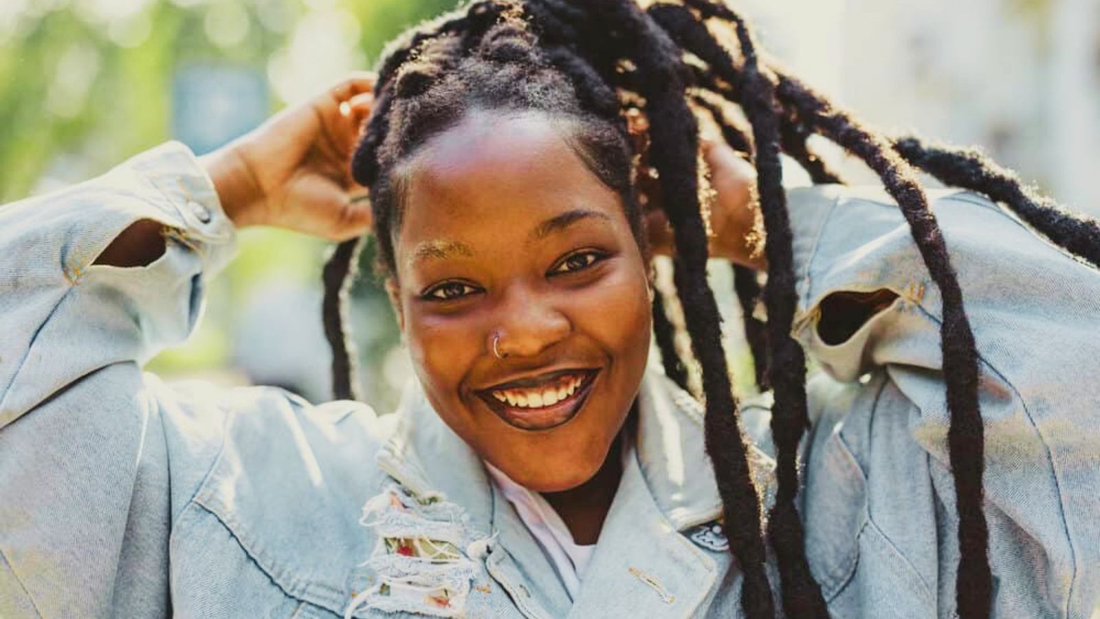 A woman with a crochet wicks hairstyle smiles while posing for a photo, showcasing her joyful expression and style.