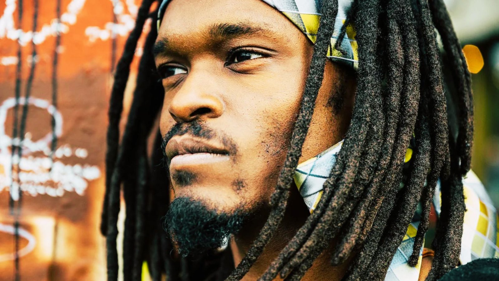 A man with dreadlocks styled in small wicks, wearing a colorful bandana on his head.